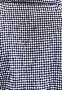 Marinblå och vit ginghamtyg med ett rutmönster med små rutor, slät textur och lätt rynkor genom hela tyget.