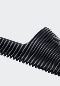 Black ribbed rubber boot with accordion-like flexible ridges, angled and curved against a plain light gray background.