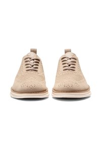 Beige Strickschuhe mit einer strukturierten Oberseite, runder Zehenpartie und tonalen Schnürsenkeln. Weiße Gummisohle mit einem leicht braunen Akzent entlang des Randes.