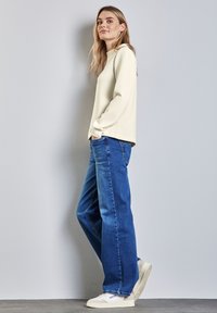 Felpa bianca a collo rotondo abbinata a jeans blu larghi e sneakers bianche. Il tessuto sembra morbido, con una vestibilità comoda e un design informale.