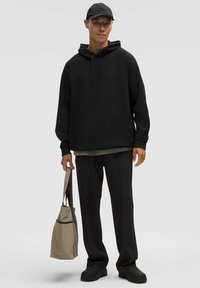 Zwarte hoodie met een trekkoord, relaxed fit, gecombineerd met zwarte broek en een beige tas. Vloeiende textuur en minimalistisch ontwerp.