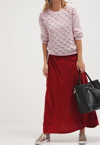 Maglione lavorato a maglia rosa chiaro con motivo a diamante, gonna maxi rossa e scarpe slip-on metalliche. Borsa a tracolla nera con dettagli testurizzati.
