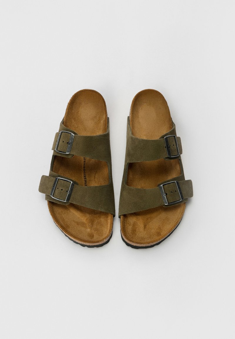 Sandales en daim vert olive avec deux boucles ajustables, semelle intérieure marron et semelle extérieure en caoutchouc texturé, conçues pour le confort et la stabilité.