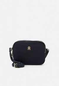 Zwarte nylon schoudertas met goudkleurig logo, ritssluiting en verstelbare riem. Rechthoekige vorm met een gladde textuur.