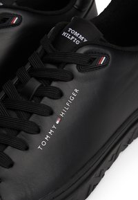 Baskets en cuir noir avec un bout arrondi, des lacets texturés et un logo sur le côté. Subtiles touches de rouge, blanc et bleu sur la languette.