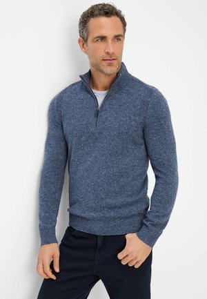 Blauer gestrickter Pullover mit einem halben Reißverschlusskragen, gerippten Bündchen und Saum, der ein strukturiertes Muster und ein figurnahes Design aufweist. Über einem grauen Shirt getragen.