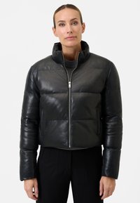 Sort læder cropped pufferjakke med ståkrave, lynlås-lukning og plysset quiltet design. Har en glat overflade og elastiske manchetter.