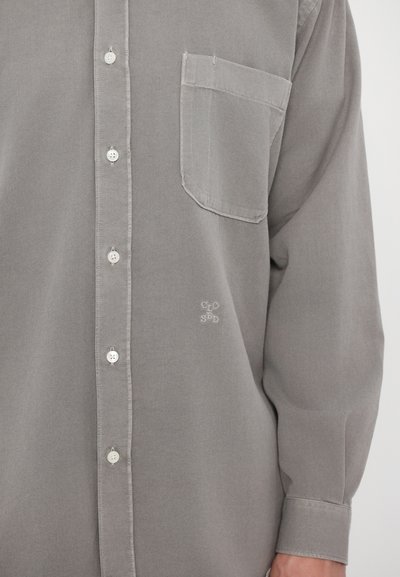 Chemise boutonnée gris clair en tissu doux. Comprend une poche poitrine et une broderie subtile près de l'ourlet. Coupe classique avec des manches longues.