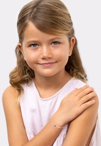 Pulsera de plata con piedras preciosas multicolores, que incluye piedras rosas, azules y transparentes, llevada en la muñeca de un niño. Top rosa claro.