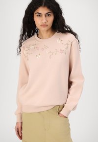 Lys rosa genser med brodert blomsterdesign i rosa og grønn, ribbet halslinning og mansjetter. Myk tekstur og avslappet passform.