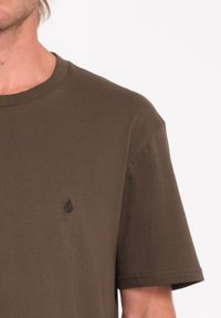 Olijfgroene katoenen t-shirt met een ronde hals en korte mouwen. Beschikt over een klein zwart logo op de linkerkant van de borst. Soepele textuur.