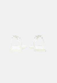 Sandales plates transparentes avec des brides transparentes et des éléments circulaires décoratifs à l'arrière du talon, vues de dos.