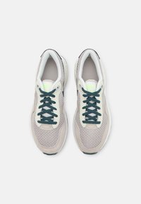 Sneaker sportive con una parte superiore in mesh beige, dettagli in suede grigio, suola intermedia bianca e lacci verdi scuri, con un dettaglio del logo verde neon.