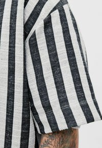 Tissu rayé gris et noir avec un motif texturé, comportant de larges rayures et une coupe ample, mettant en valeur la finition des manches.
