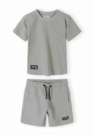 Jasnoszara koszulka z krótkim rękawem o splocie waflowym oraz szorty z elastyczną talią i czarnym sznurkiem oraz czarnymi naszywkami po lewej dolnej stronie.