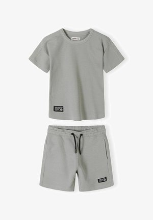 Jasnoszara koszulka z krótkim rękawem o splocie waflowym oraz szorty z elastyczną talią i czarnym sznurkiem oraz czarnymi naszywkami po lewej dolnej stronie.