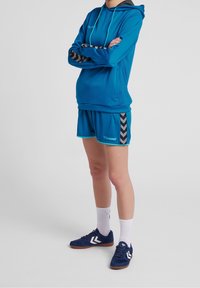 Niebieska sportowa bluza z kapturem i szorty z czarnymi akcentami w zygzak, w połączeniu z niebieskimi butami i białymi skarpetami. Skoncentrowanie się na sportowym designie i materiale.