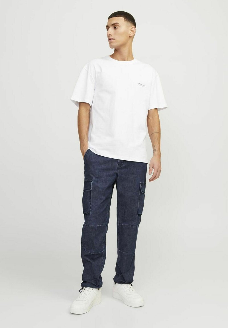 Tricou alb din bumbac cu mâneci scurte și guler rotund, asociat cu pantaloni cargo bleu închis, cu mai multe buzunare și o croială lejeră.