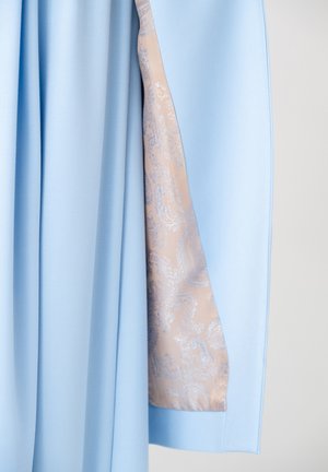 Jasnoniebieska tkanina ułożona w fałdy odsłania beżową podszewkę z błyszczącym srebrnym wzorem paisley wewnątrz ubrania.