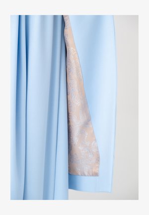 Jasnoniebieska tkanina ułożona w fałdy odsłania beżową podszewkę z błyszczącym srebrnym wzorem paisley wewnątrz ubrania.