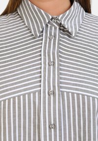 Chemise à boutons rayée gris et blanc. Dotée d'un col classique, de six boutons et d'une texture lisse avec des rayures verticales de largeurs variées.