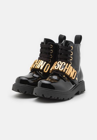 Bottines en cuir verni noir avec logo en métal doré, bout rond, lacets à l'avant et semelle rugged pour une meilleure adhérence.