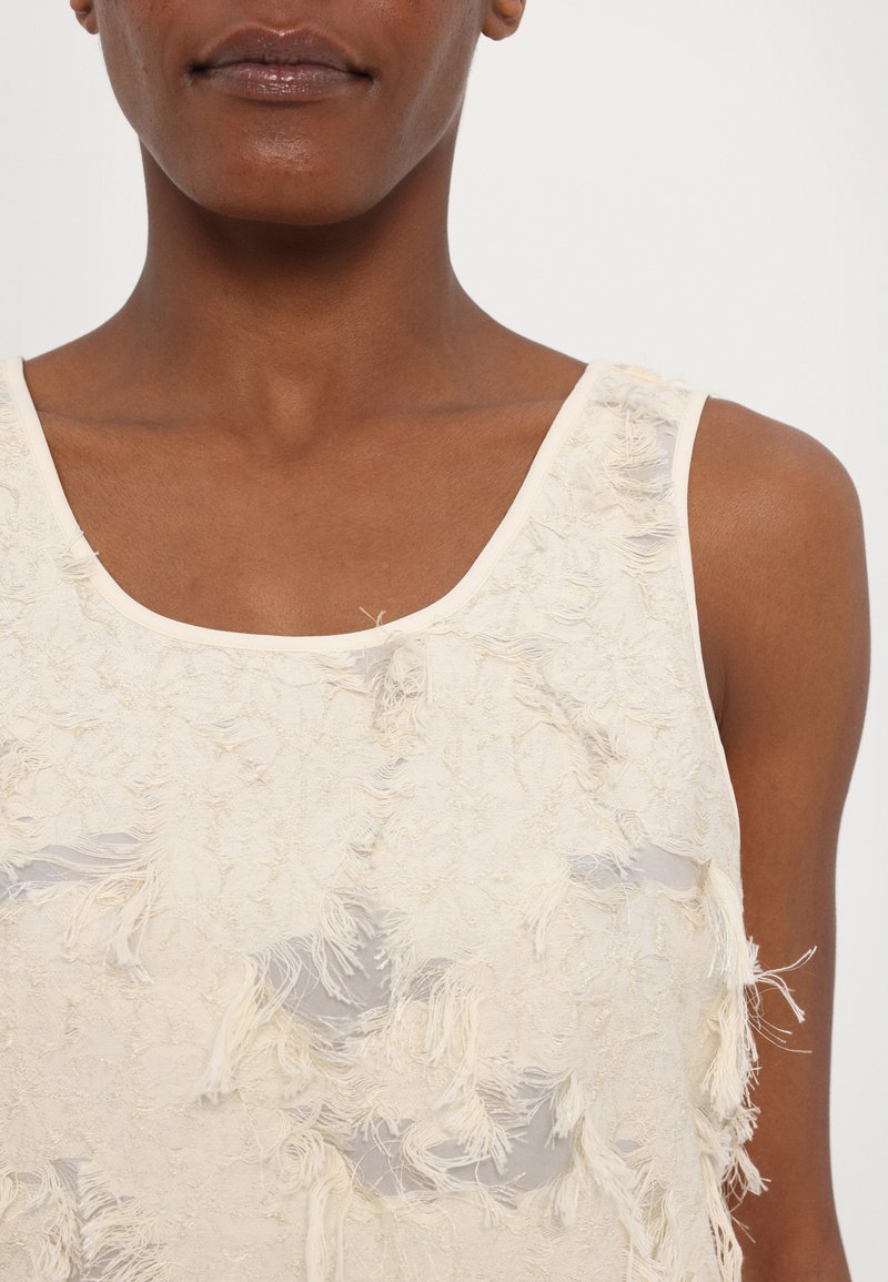 Crème tanktop met een textuur oppervlak met rafelige accenten; ronde halslijn; dunne bandjes; zachte, lichte stof.