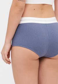 Blå stripete høytaljede truser med en hvit elastisk midje. Stoffet ser mykt ut med en teksturert overflate og sømløse kanter.