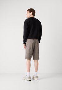 Černá mikina s kulatým výstřihem, spárovaná s béžovými šortkami končícími nad koleny. Model má na sobě světlé tenisky a bílé ponožky.