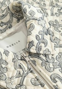 Kurtka pikowana z kościelnobiałej tkaniny z niebieską kwiatową haftem, zapinana na zamek, z metką "NOELLA".