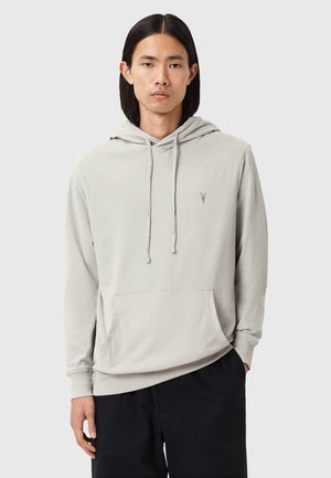 Haut en coton gris clair avec une poche kangourou à l'avant, une capuche à cordon de serrage et un petit logo brodé sur le côté gauche de la poitrine. Design simple.