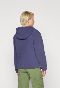 Granatowy polarowy hoodie z teksturowaną powierzchnią, z kapturem, w połączeniu z zielonymi spodniami cargo. Styl jest swobodny i luźny.