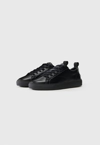 Black leather sneakers feature a smooth texture, rounded toe, flat soles, and front lacing with a pull tab on the heel.