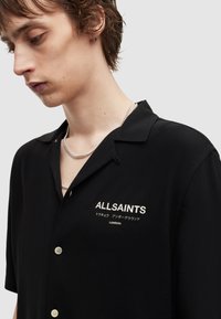Black short-sleeve shirt made of smooth fabric, featuring a button-up design, embroidered logo in white, and a notched collar.