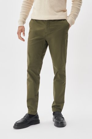 Olive green, straight-leg trousers with a smooth texture, featuring a front pocket and subtle stitching. Paired with black slip-on shoes.