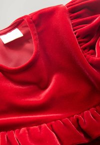 Abito in velluto rosso con scollo rotondo, dettagli arricciati sulle spalle e orlo increspato. Texture liscia con un colore ricco e intenso.
