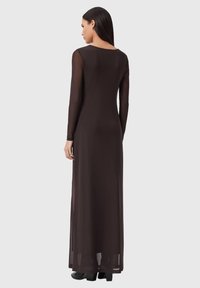 Langes, bodenlanges Kleid in Dunkelbraun mit glatter Textur und einem schlichten Rundhalsausschnitt, mit transparentem Stoff an den Ärmeln.