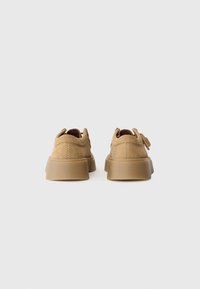 Paire de chaussures à plateforme en daim beige vues de dos sur un fond clair uni.