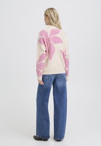 Pull clair avec un grand motif floral rose sur le dos et les manches, associé à un jean bleu ample. Texture douce et coupe décontractée.