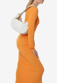 Borsa a spalla in pelle bianca con una forma arrotondata, dettaglio in piping nero e una singola tracolla regolabile, indossata su un vestito arancione a coste.