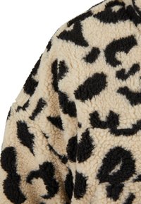 Tessuto in pile fantasia leopardo beige e nero, con superficie morbida e texture, caratterizzato da macchie nere irregolari che creano un aspetto accogliente.