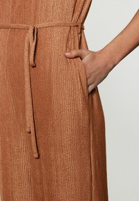 Vêtement couleur rouille avec une texture côtelée, doté d'une taille nouée et de poches latérales, mettant en valeur un tissu lisse et doux.