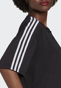 Black t-shirt with short sleeves, featuring three white stripes along the shoulder seam. Fabric appears smooth with a relaxed fit.