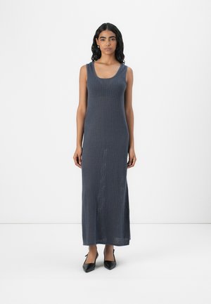 Gray knitted maxi dress with a scoop neckline, textured pattern, sleeveless design, and side slits, paired with black pointed shoes.