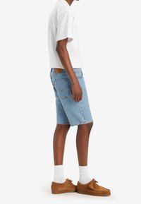 Shorts de mezclilla azul clara con un corte recto, cinco bolsillos y una etiqueta de cuero marrón en la parte trasera, combinados con una camiseta blanca y zapatos marrones.