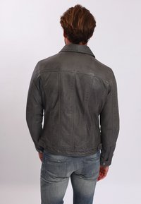 Šedá kožená bunda s klasickým límcem a vertikálním švem. Obsahuje patentky a přiléhavý střih, kombinovaná s modrými džíny.