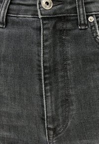 Jeans de algodón negro con una vista en primer plano de la textura de la tela, detalles de costura y un botón de metal plateado en la cinturilla.