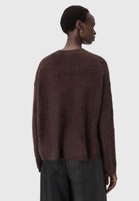 Brauner, flauschiger Strickpullover mit lockerer Passform, herabgesetzten Schultern und rundem Ausschnitt. Kombiniert mit schwarzen, glatt strukturierten Hosen.