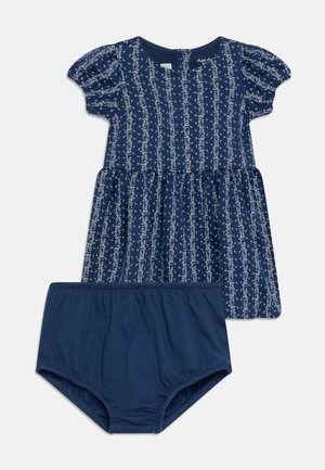 Rochie navy cu mâneci bufante, model floral alb și talie strânsă; include pantaloni scurți navy asortați. Material din bumbac, textură netedă.