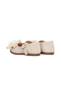 Zapatos de tela beige con superficie texturizada, presentan un acento floral y una hebilla lateral. Suela blanda y forma redondeada para mayor comodidad.